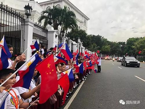 20日，來自馬尼拉當地三所小學的千名小學生站在總統府道路兩側揮舞兩國國旗，歡迎習主席車隊。（圖片來源：中央廣播電視總臺央視新聞 記者鄧雪梅拍攝）